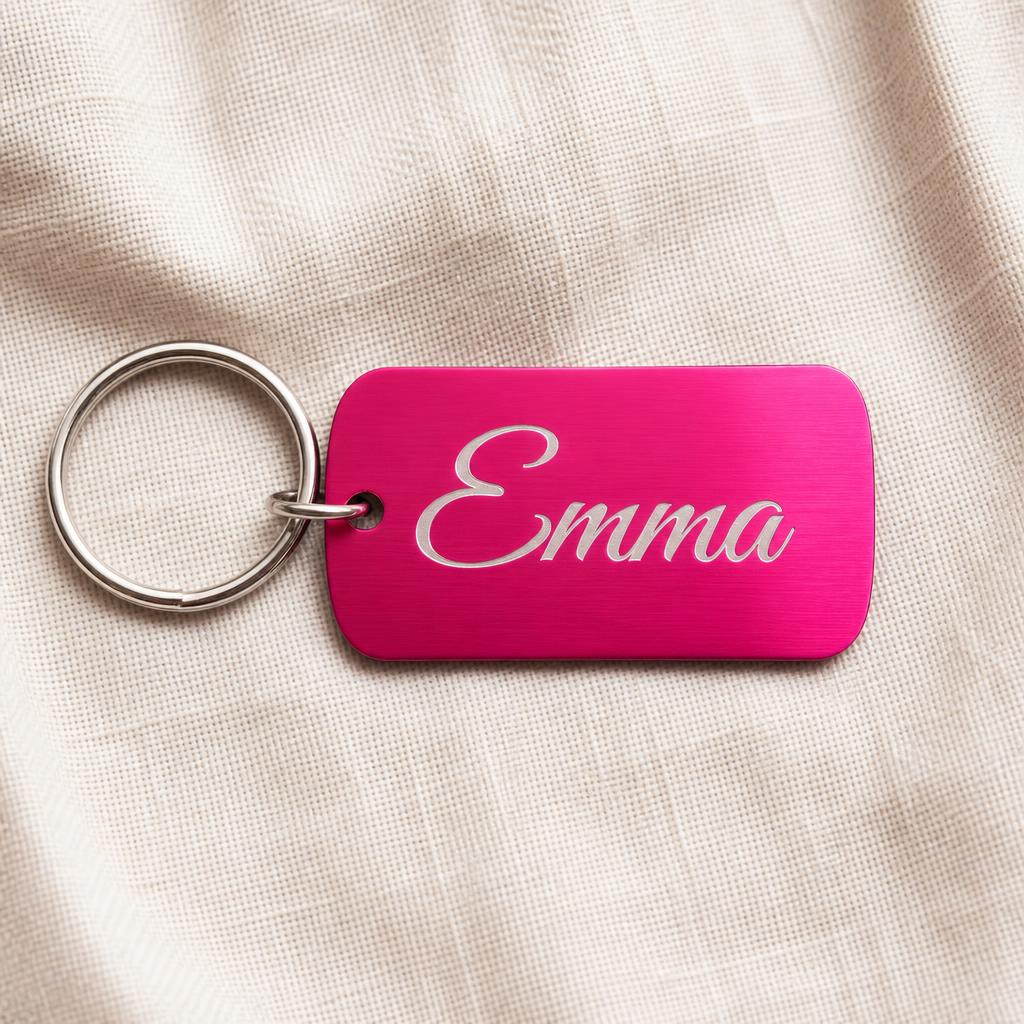 Hot Pink anodized aluminum laser-engraved keychain with the name Emma in script — the engraving reveals bare sanded aluminum — on cream linen